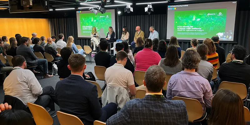 Photo from Climate Week Zurich showing a panel discussion with five speakers seated on stage before Picterra presentation slide on climate risk and supply chain resilience, with an audience listening in the foreground.